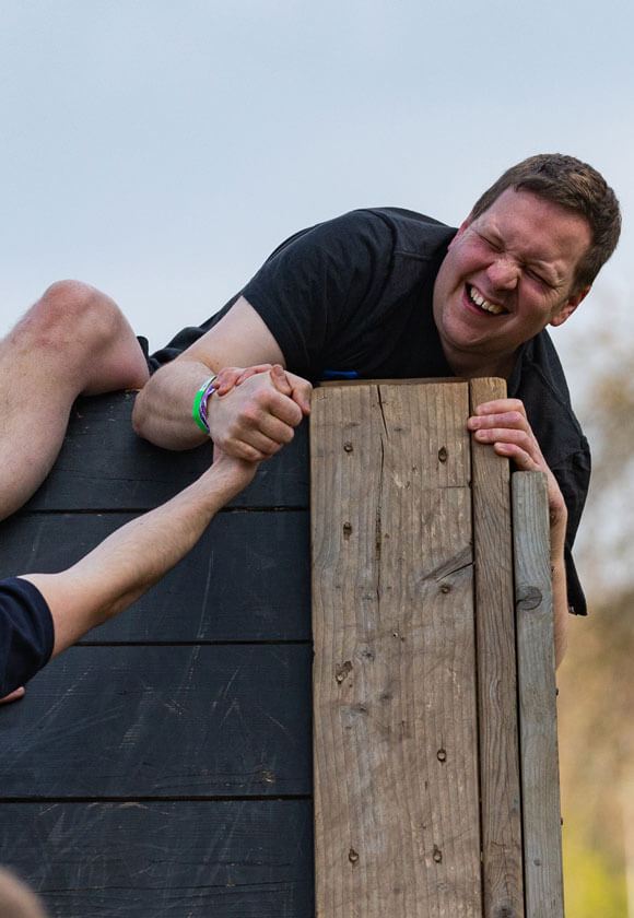Participant holding the hand of his teammate while holding tightly on a wood